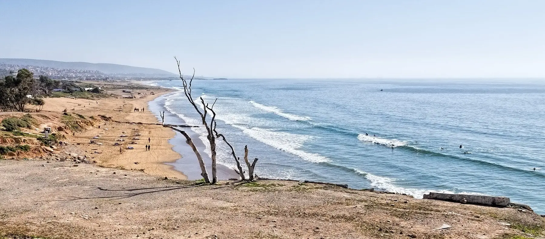 Surfers in the water off a long sandy beach on the Taghazout coast